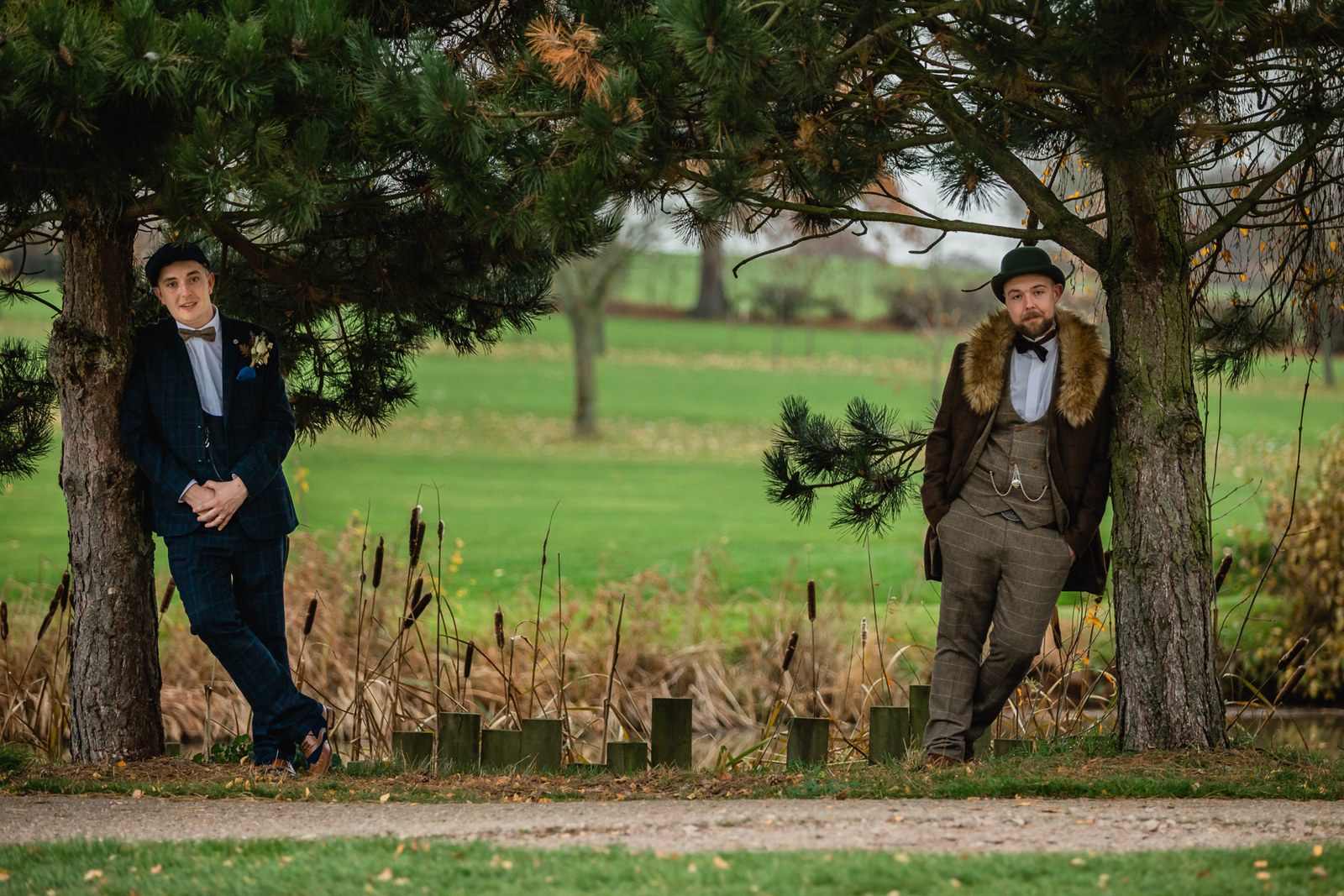 The grooms leaning against a tree beside the lakeside reeds