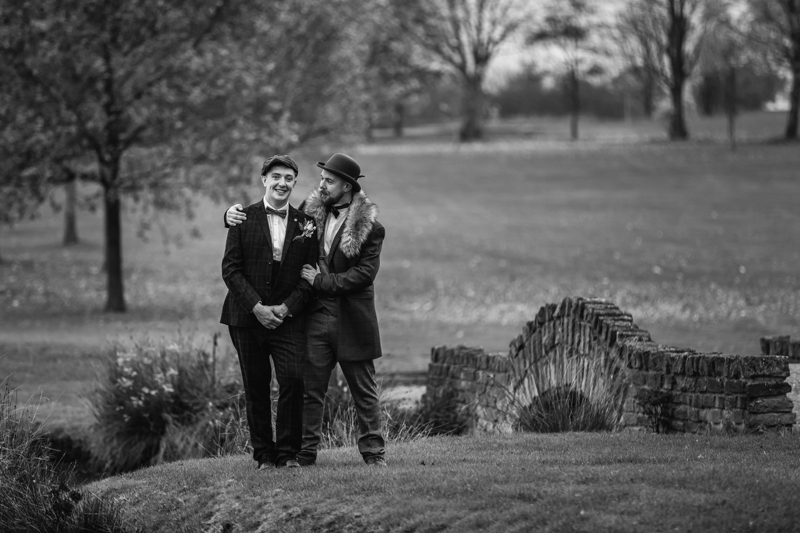 Black and white portrait of the grooms beside a dry-stone wall