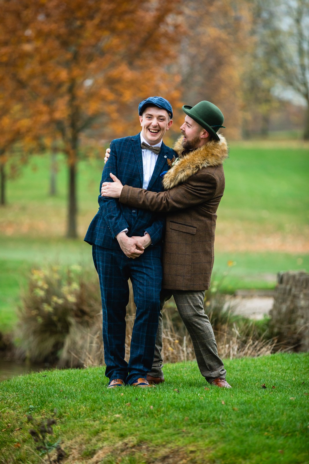The two grooms embracing on the lawn amid autumn trees