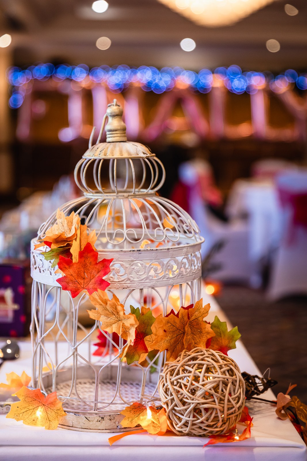 Reception centrepiece of a white birdcage trimmed with autumn leaves