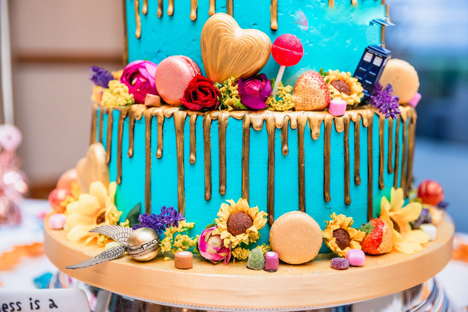 Close-up of the teal drip wedding cake with sunflowers and macarons