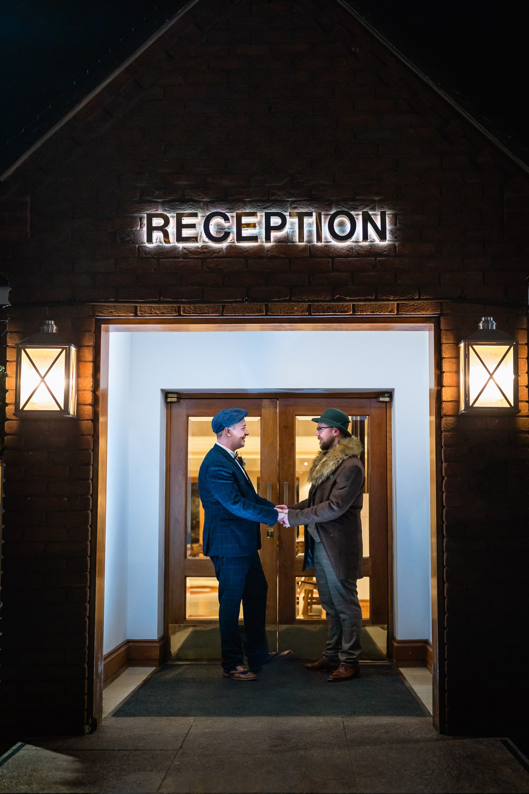 The grooms greeting beneath the lit reception sign at Windmill Village Hotel