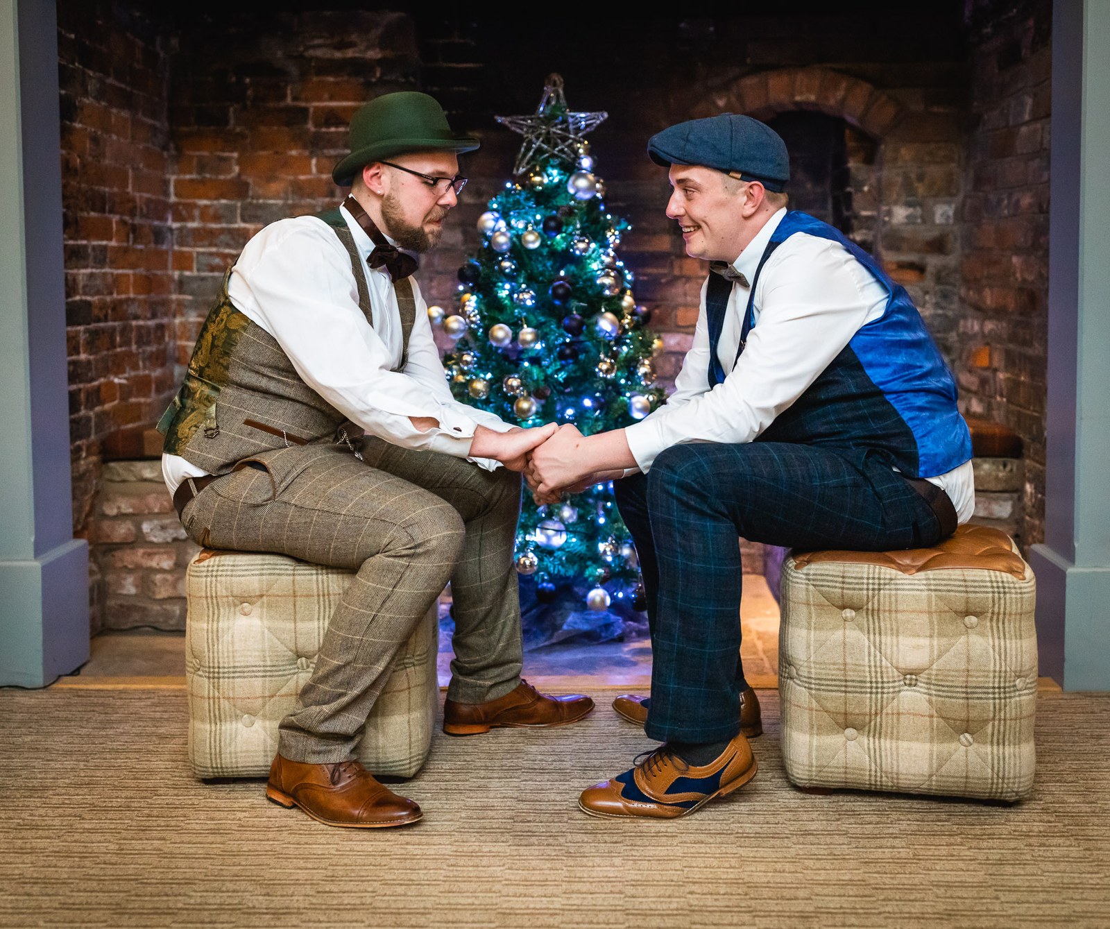 The grooms seated on checked tweed stools beside a decorated Christmas tree
