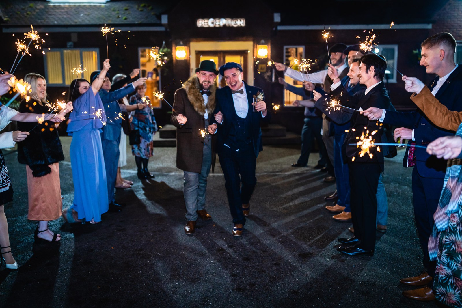 The grooms walking through a sparkler send-off outside the venue at night