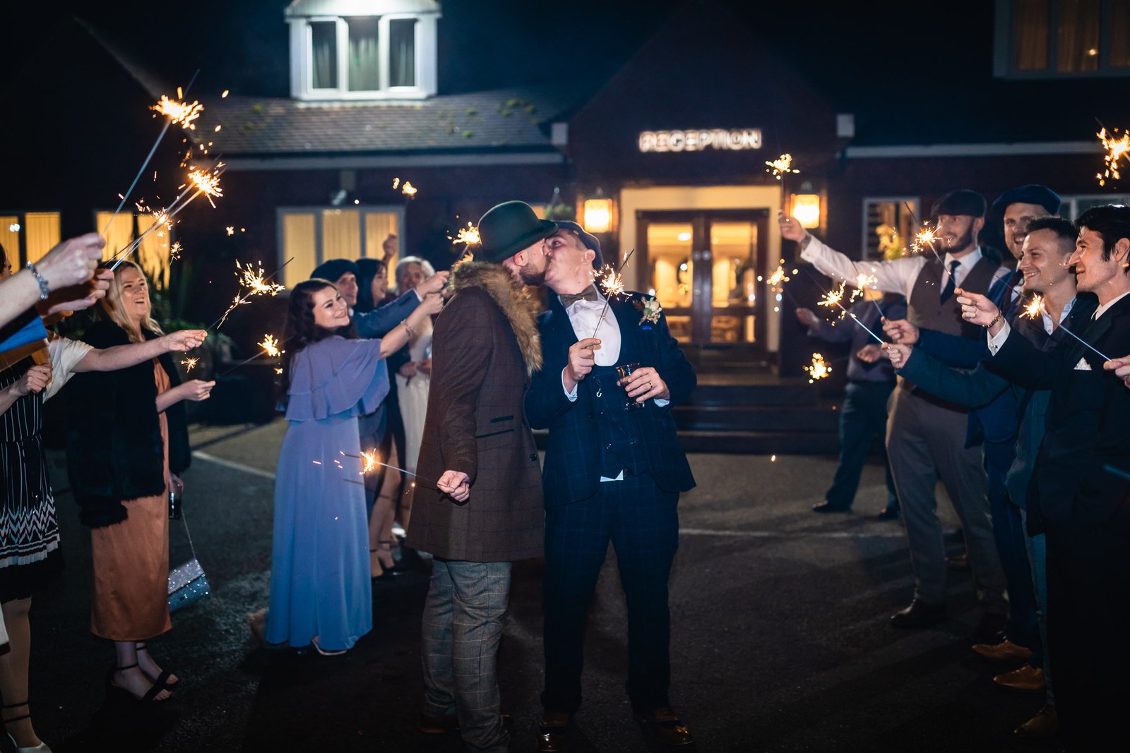 The two grooms kissing amid sparklers outside the reception