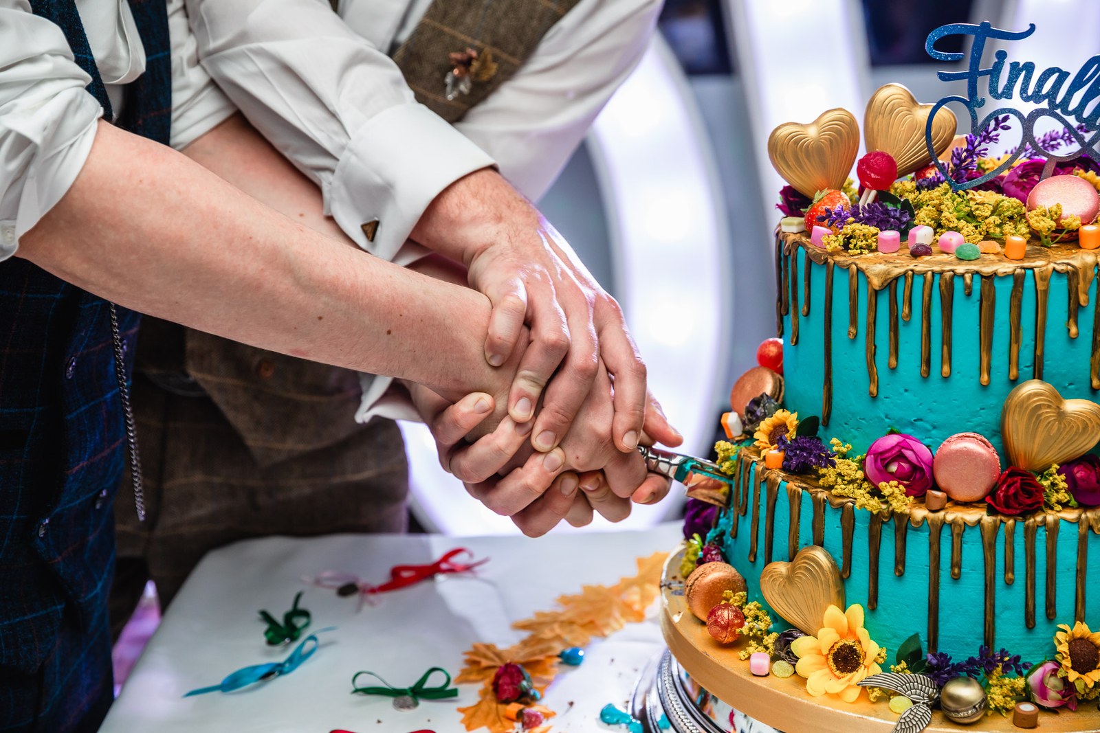 Close-up of the grooms' hands cutting their two-tier wedding cake