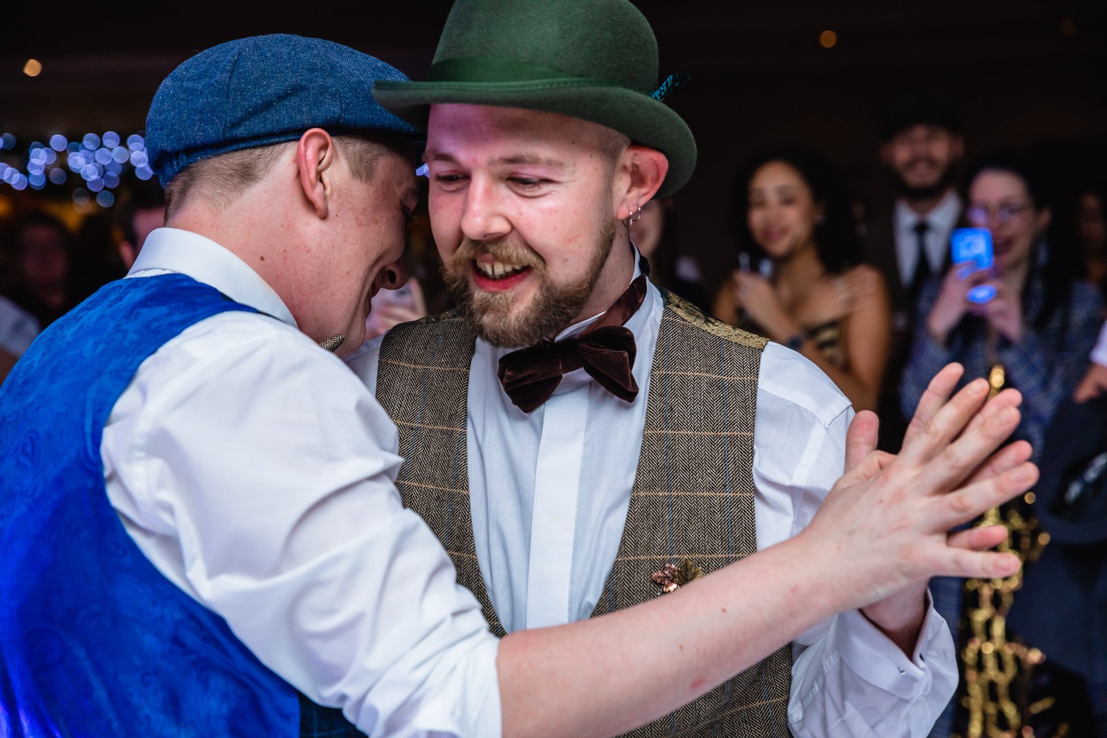 The two grooms dancing closely together as guests film