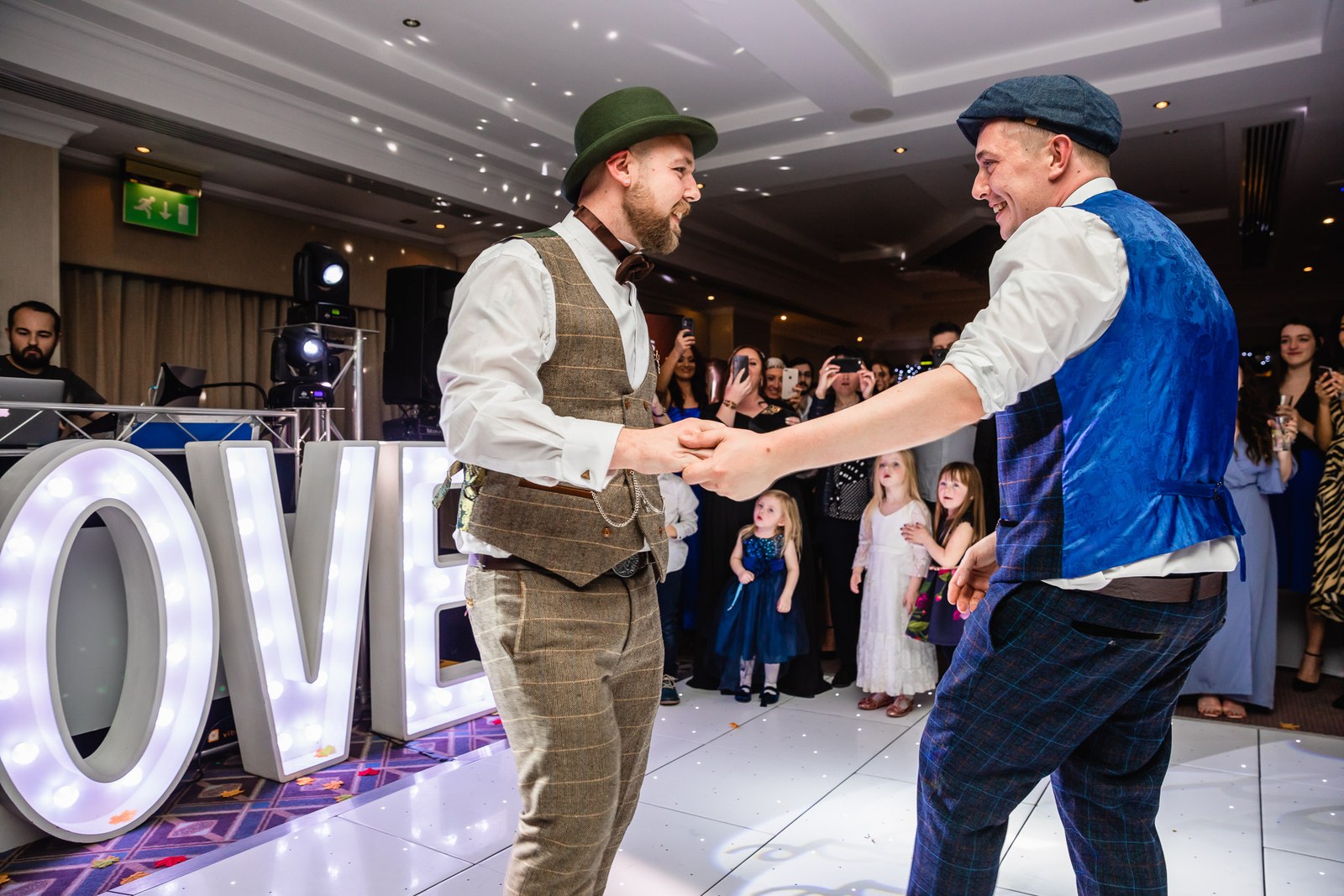 The two grooms dancing hand in hand by the illuminated letters