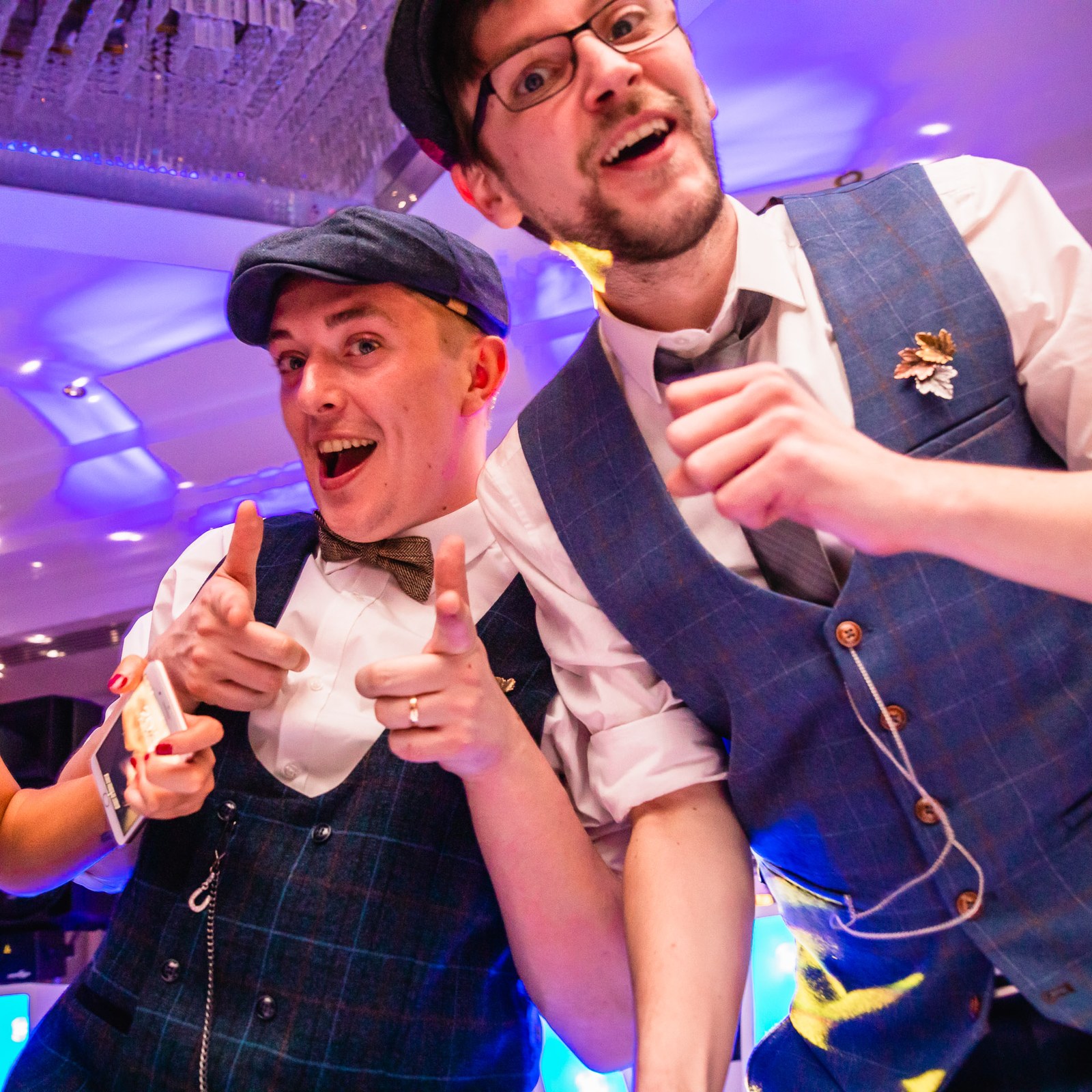 A groom and a guest pointing and laughing towards the camera while dancing