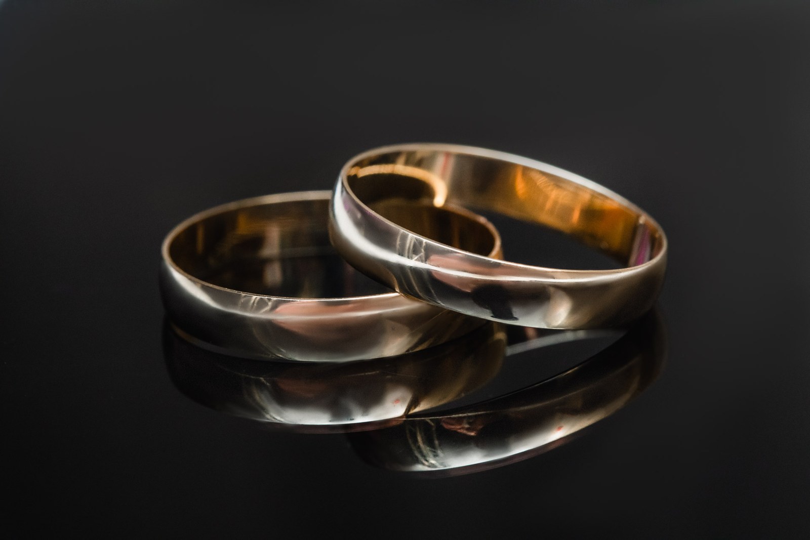 Two gold wedding bands resting on a dark reflective surface