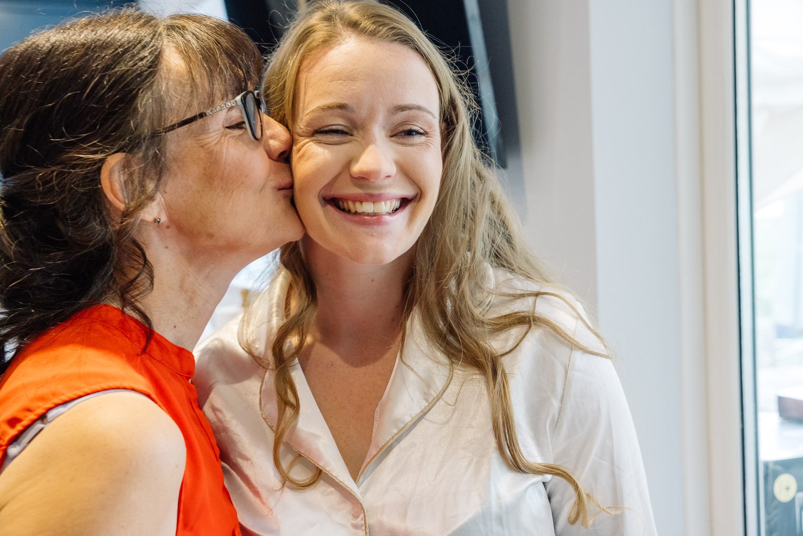 The bride's mother kissing her cheek as she smiles during the morning preparations