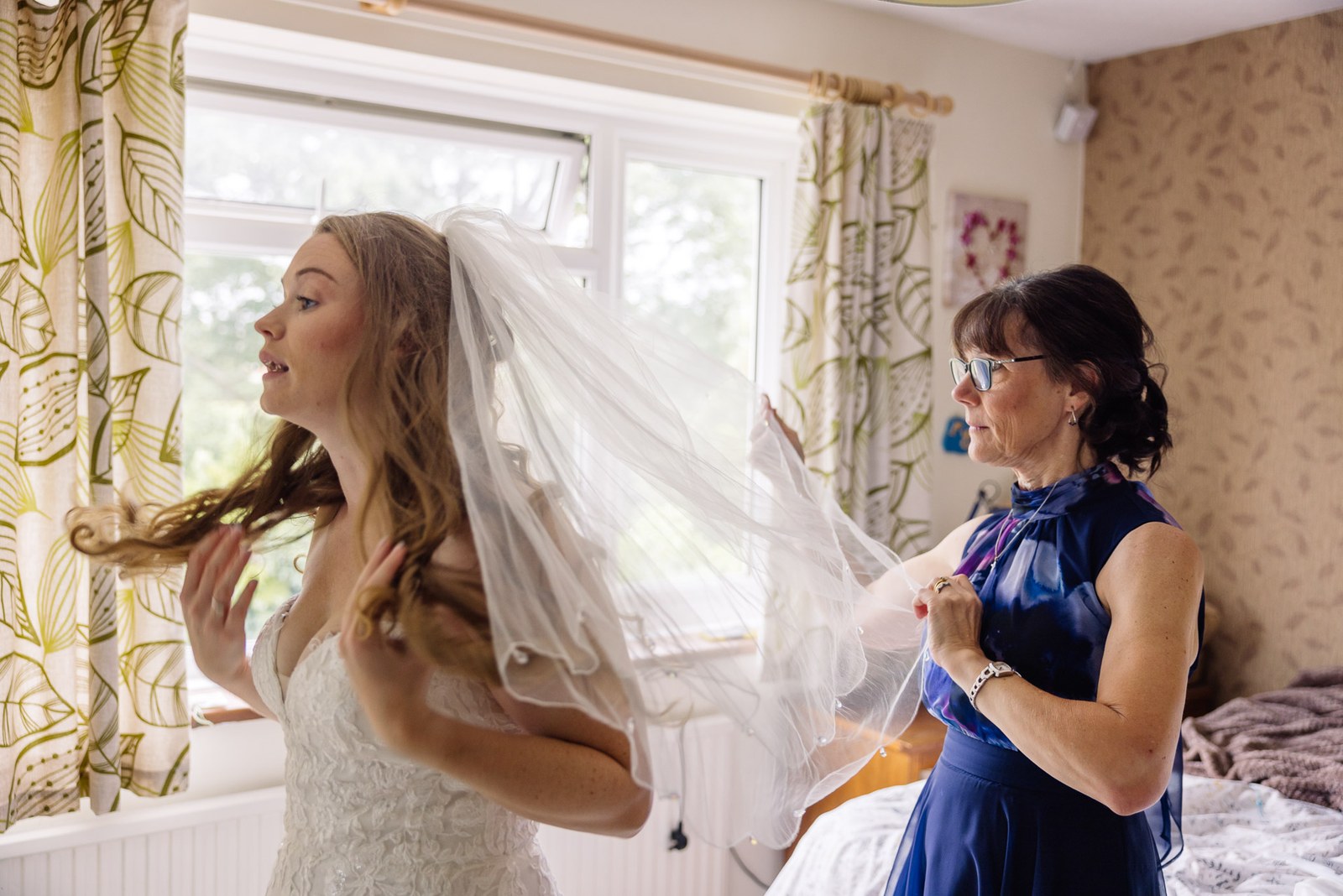 The bride's mother helping to arrange her veil beside the window