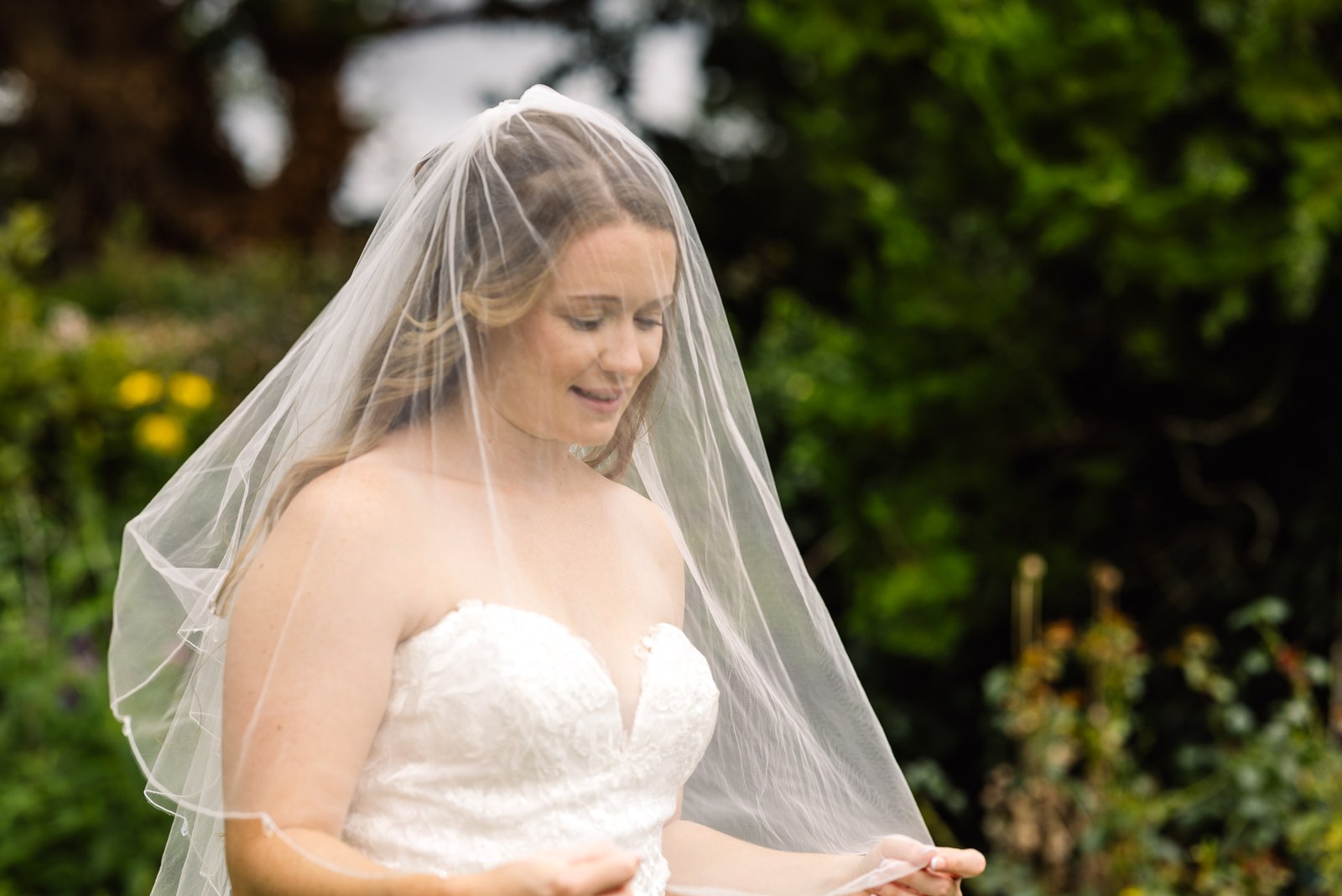 Bride in her veil looking down amid the leafy greenery