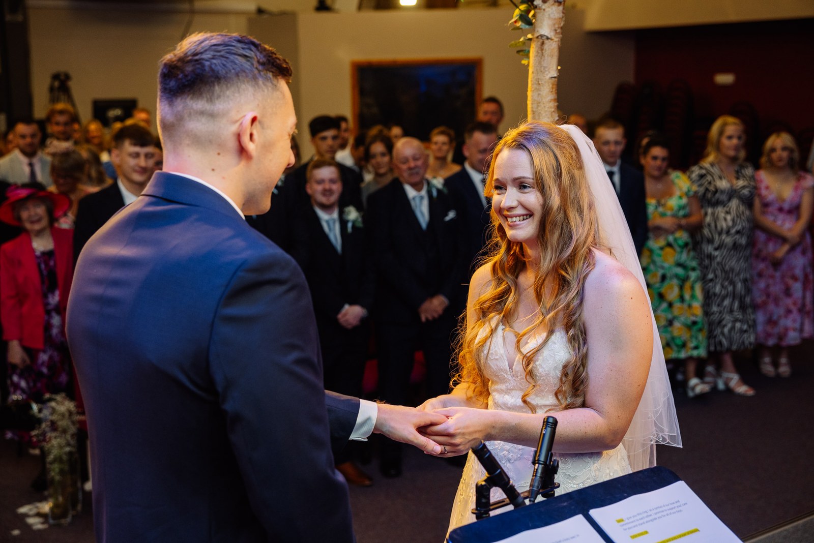 The couple holding hands during their ceremony as guests stand