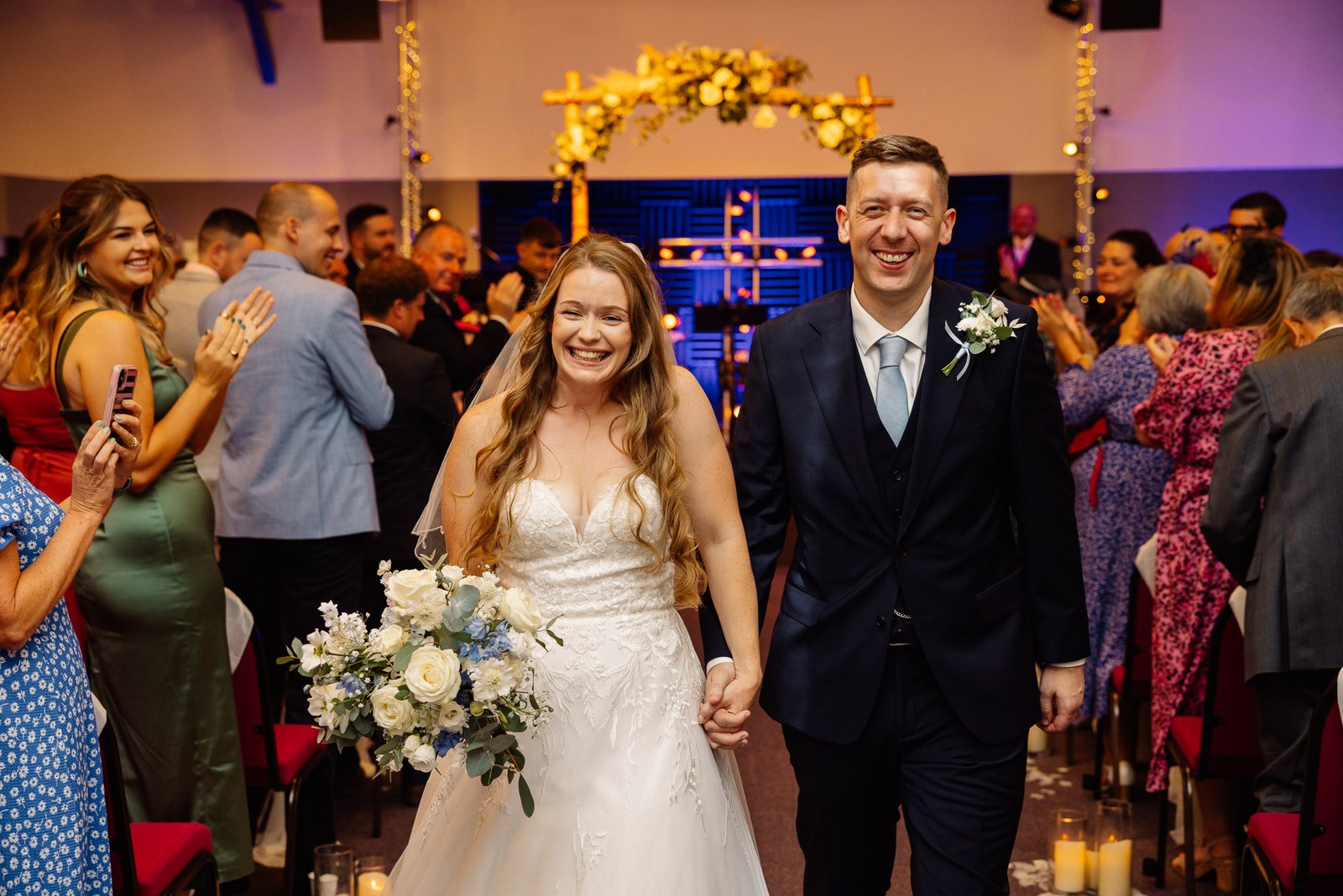 Newlyweds walking back up the aisle as guests applaud
