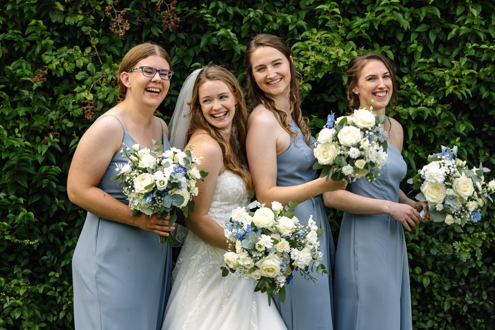 Bride with her bridesmaids and bouquets beside an ivy-clad wall