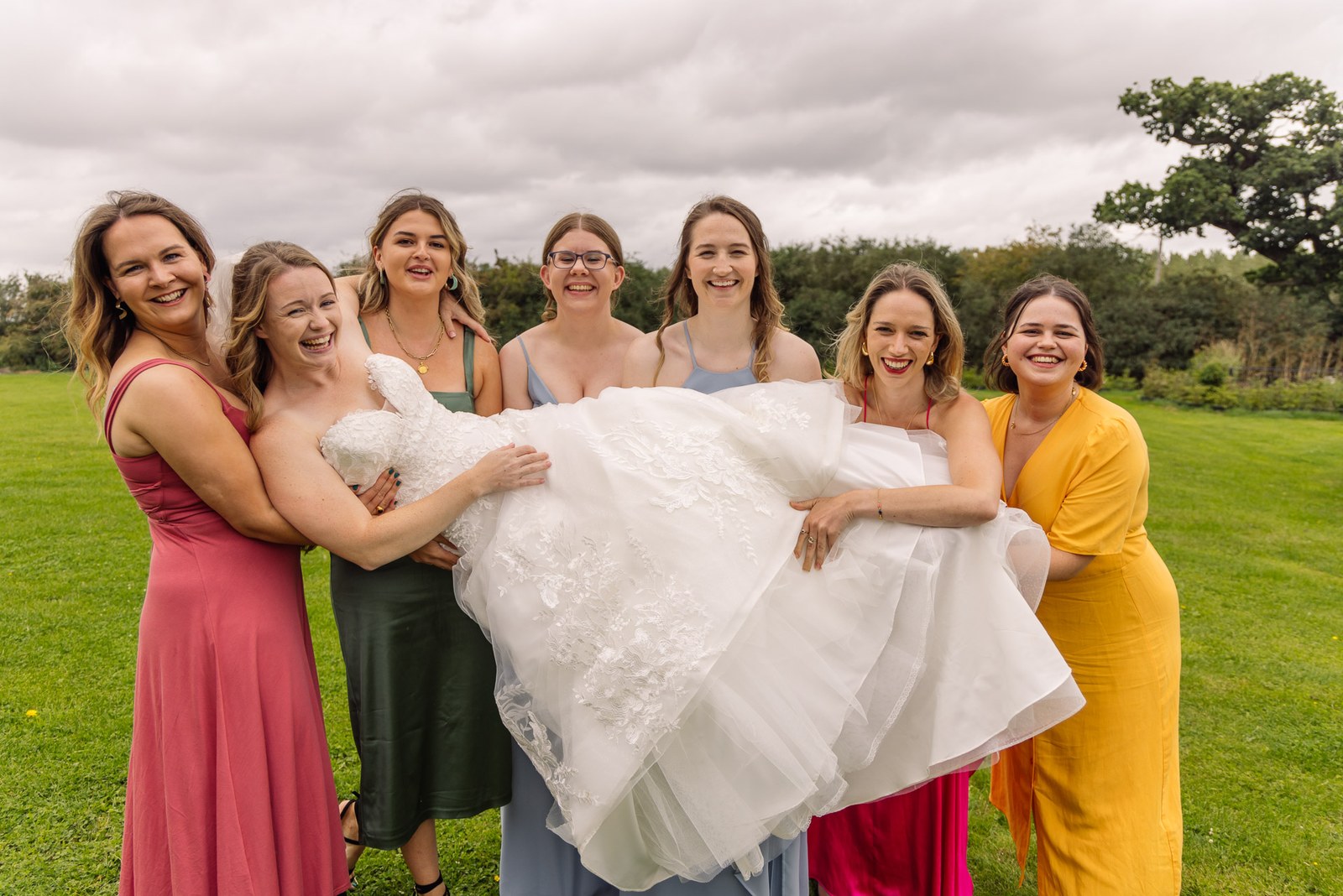 Bridesmaids and guests playfully lifting the laughing bride on the lawn