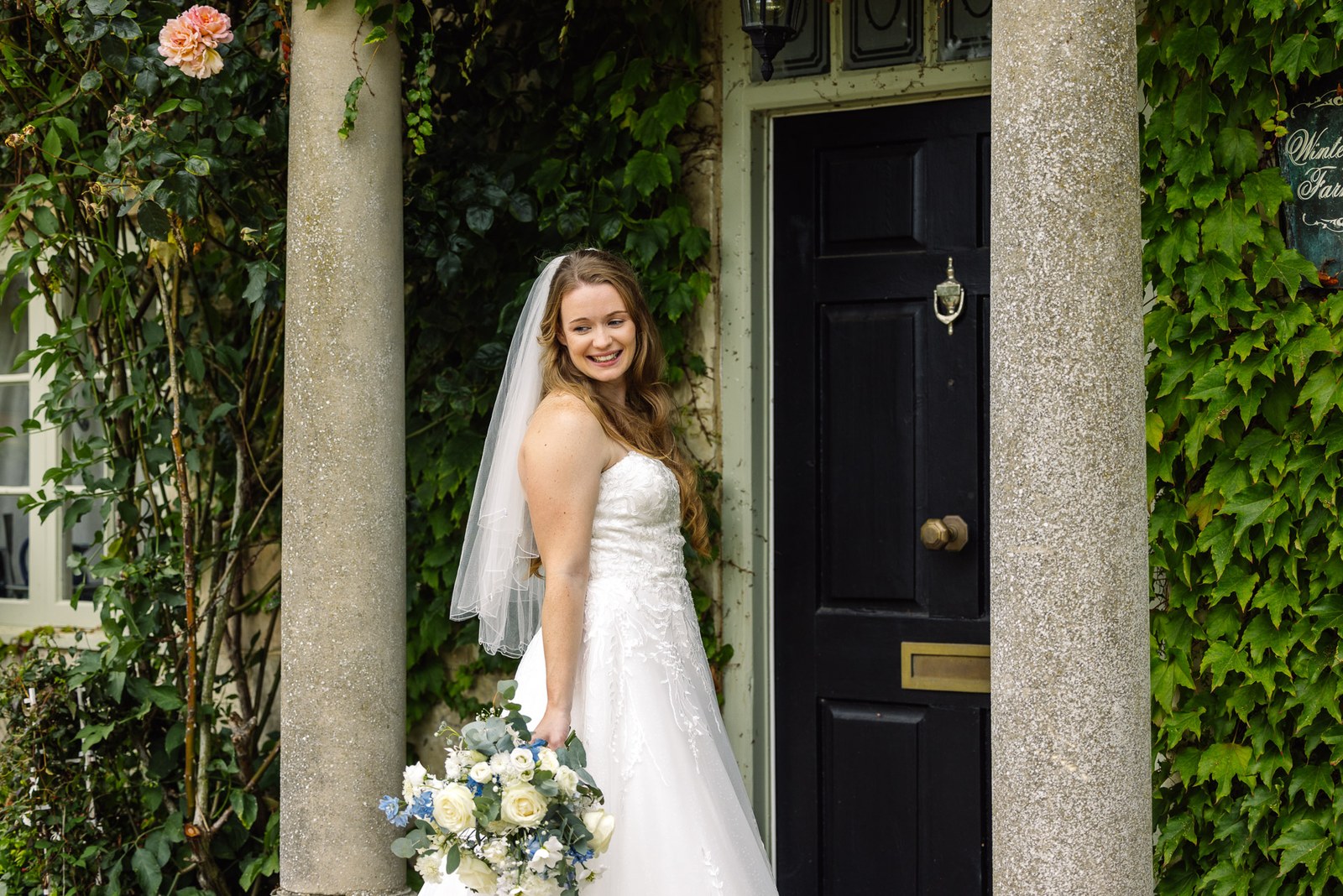 Bride posing by an ivy-framed black doorway with her bouquet