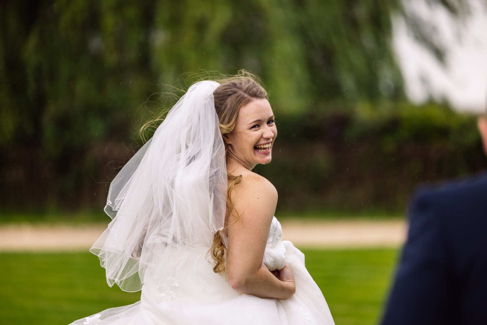 Bride laughing over her shoulder in her veil on the lawn