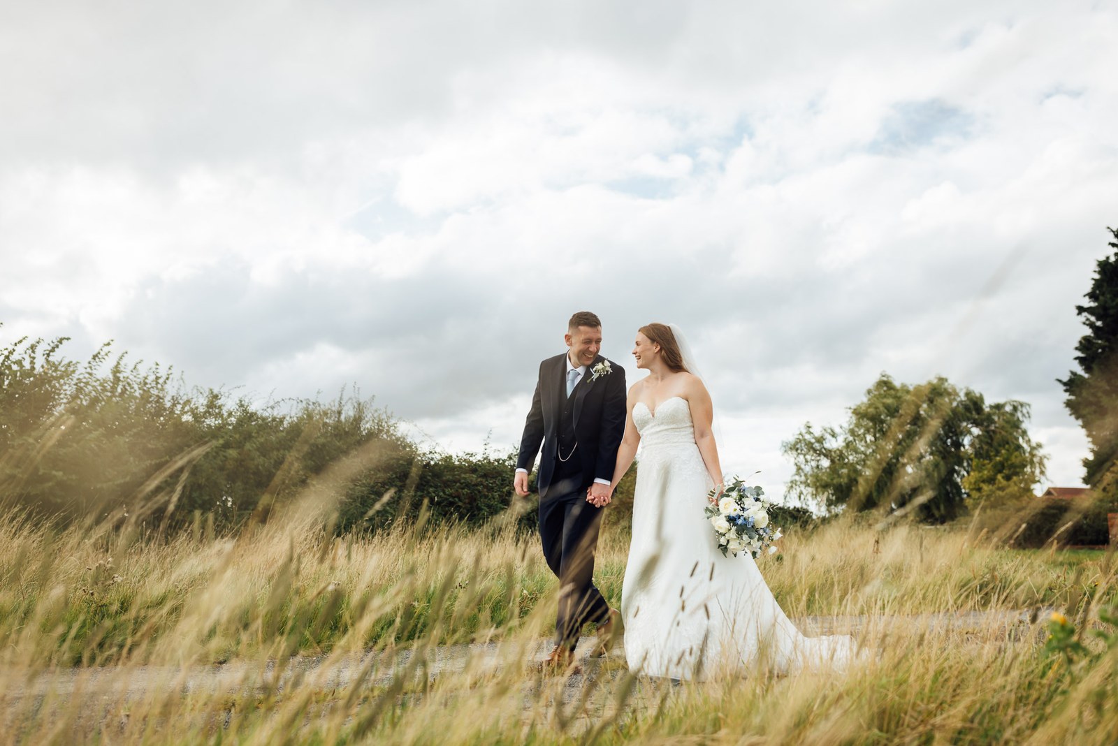 The couple walking hand in hand through a meadow at Winters Tale Country Barn
