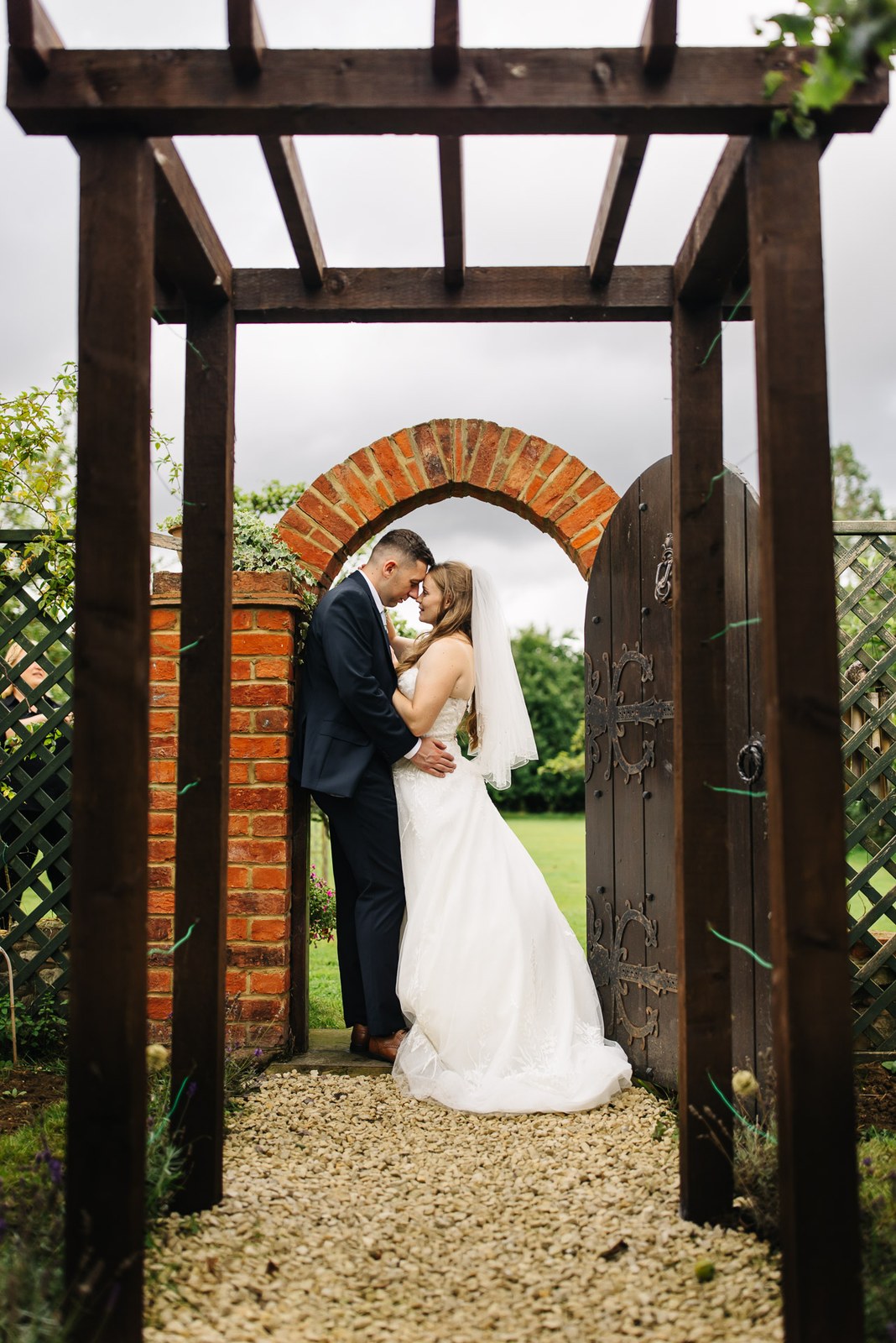 The newlyweds embracing under the pergola gateway to the garden