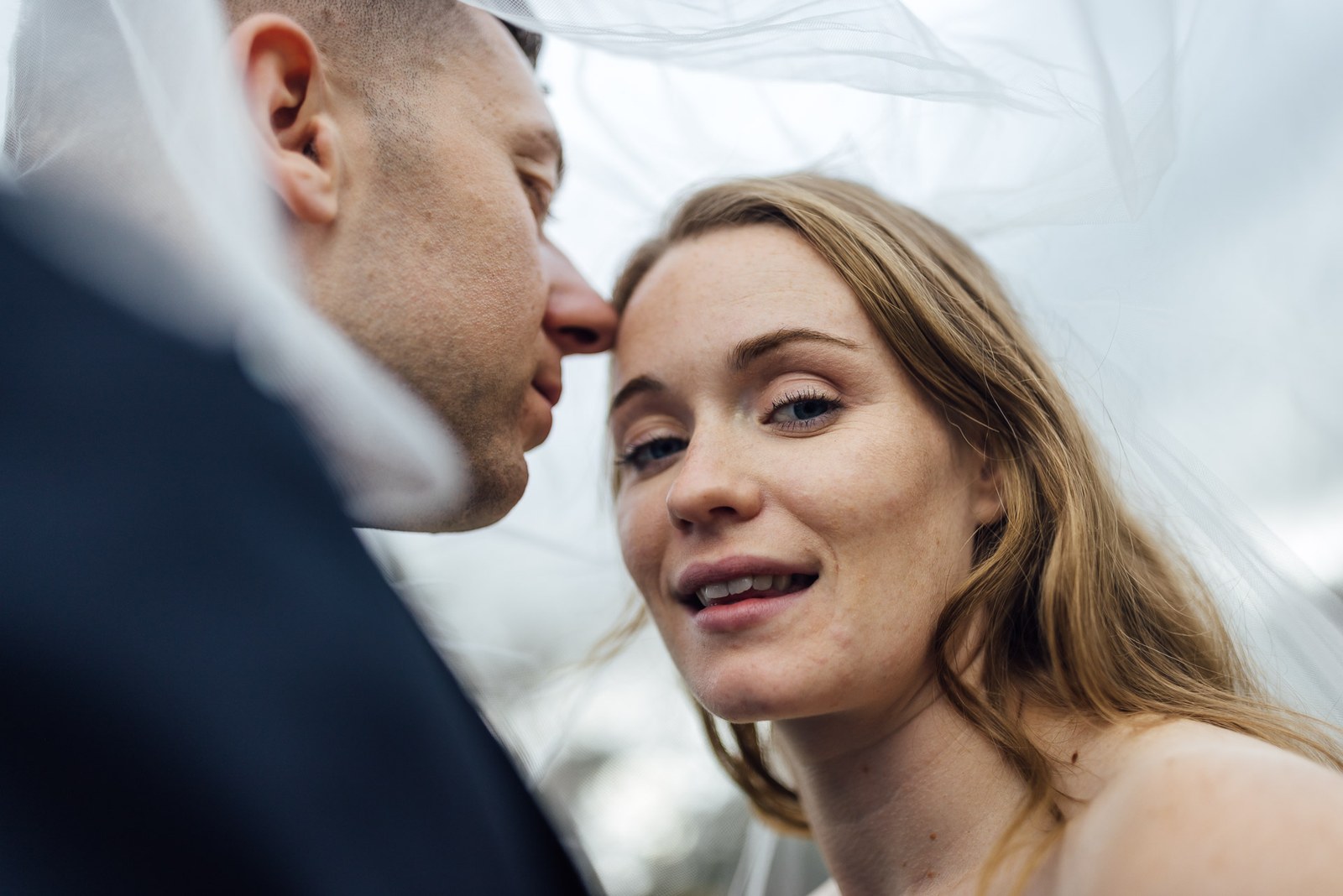 Close-up of the couple beneath the veil as the groom kisses her temple