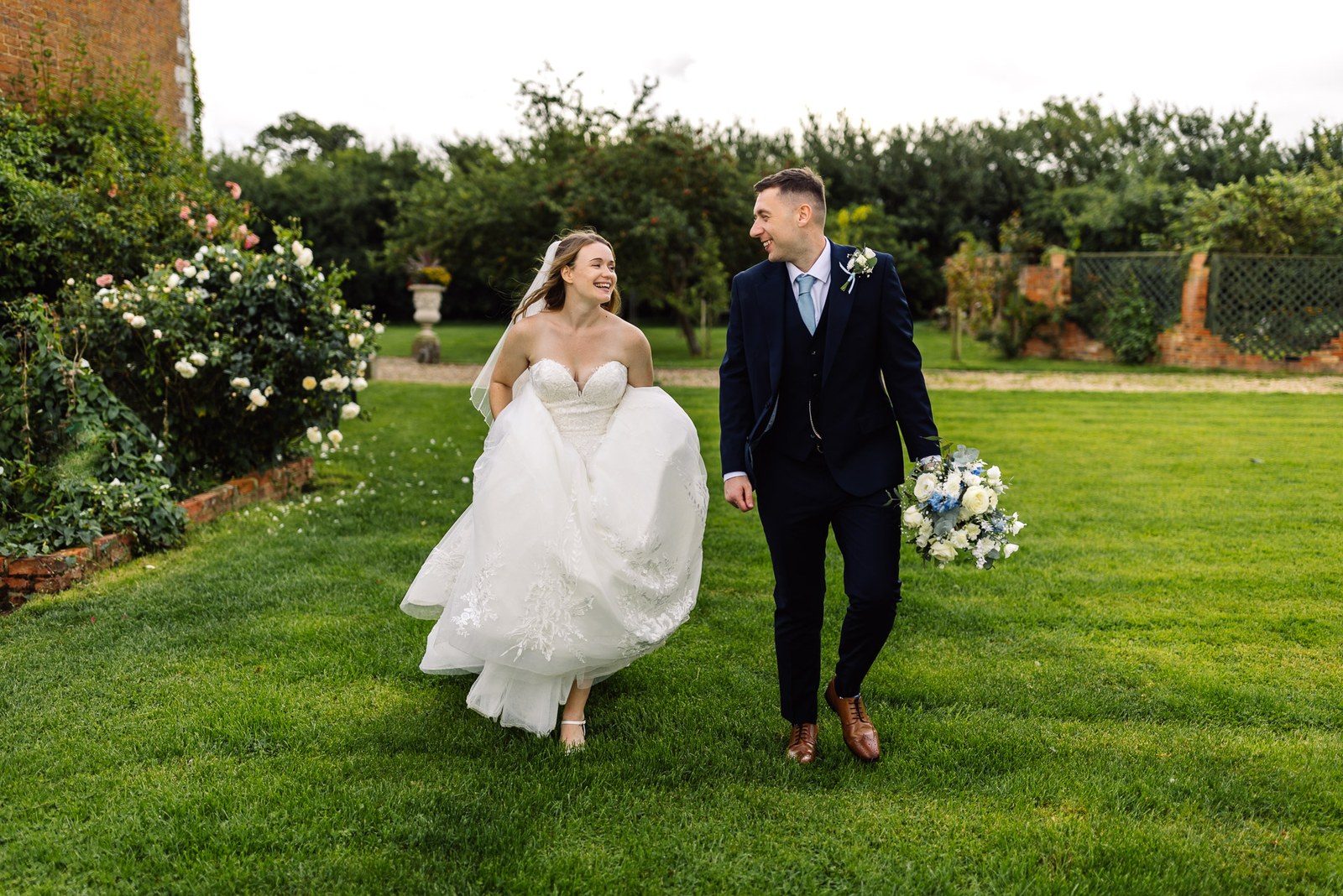The couple crossing the garden lawn at Winters Tale Country Barn past rose borders