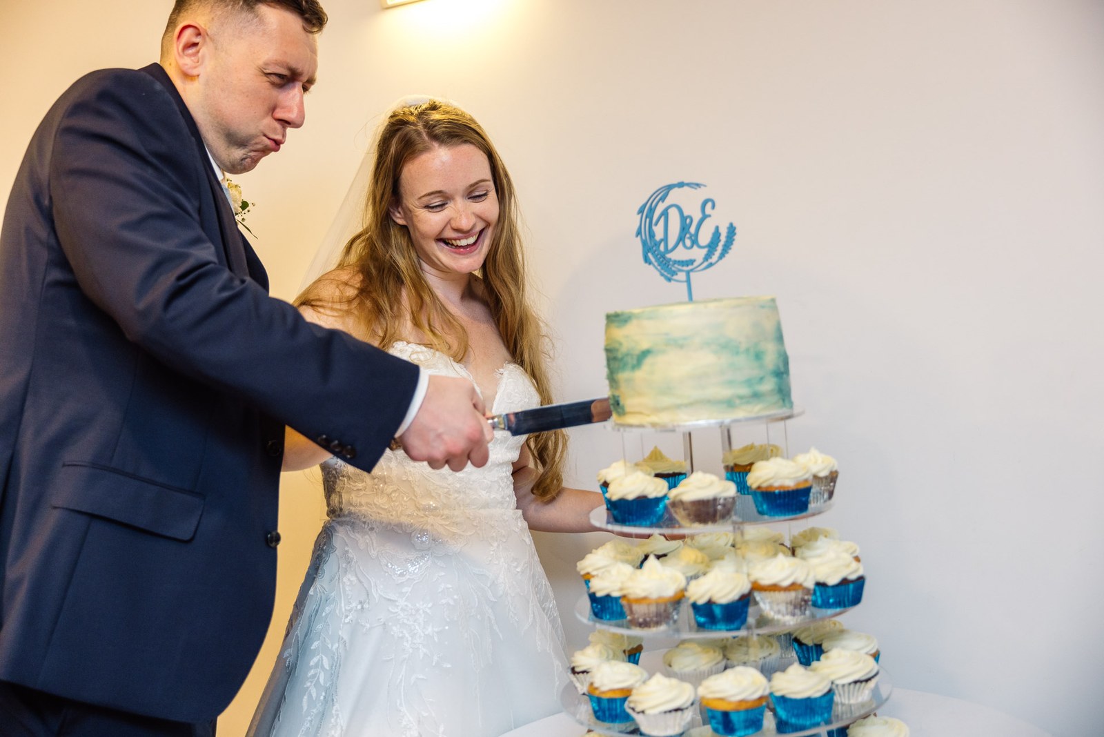 Bride and groom cutting their watercolour cake set atop a tower of cupcakes