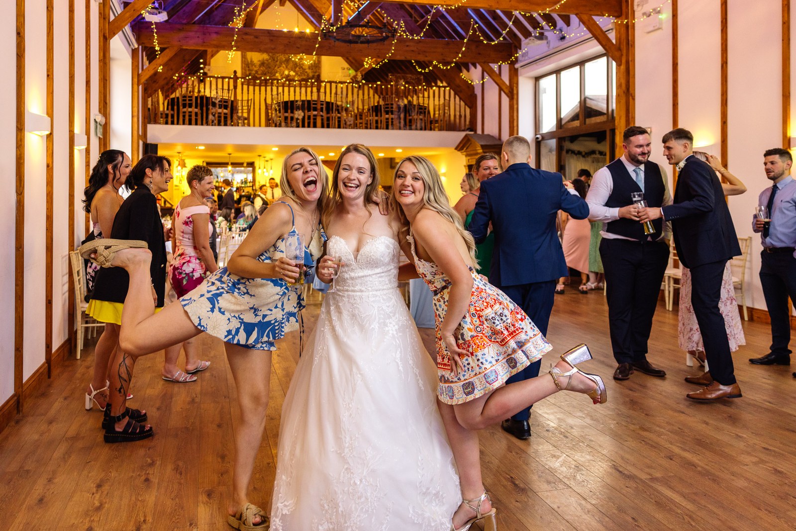 Bride dancing and laughing with friends beneath the barn fairy lights