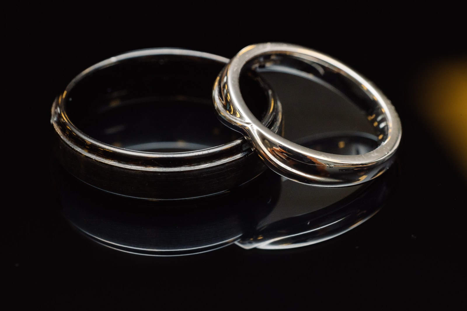 Two wedding bands resting together on a dark reflective surface
