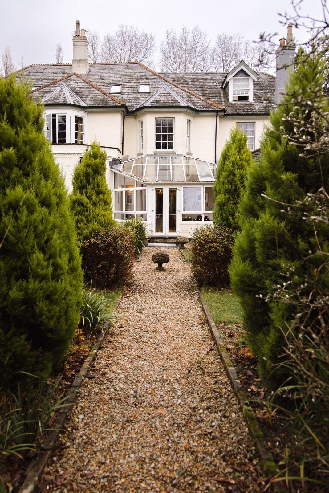 The white period facade of Woodlands Lodge Hotel down a conifer-lined gravel path