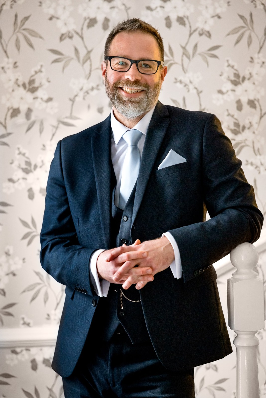 Portrait of the groom in his navy suit beside the staircase