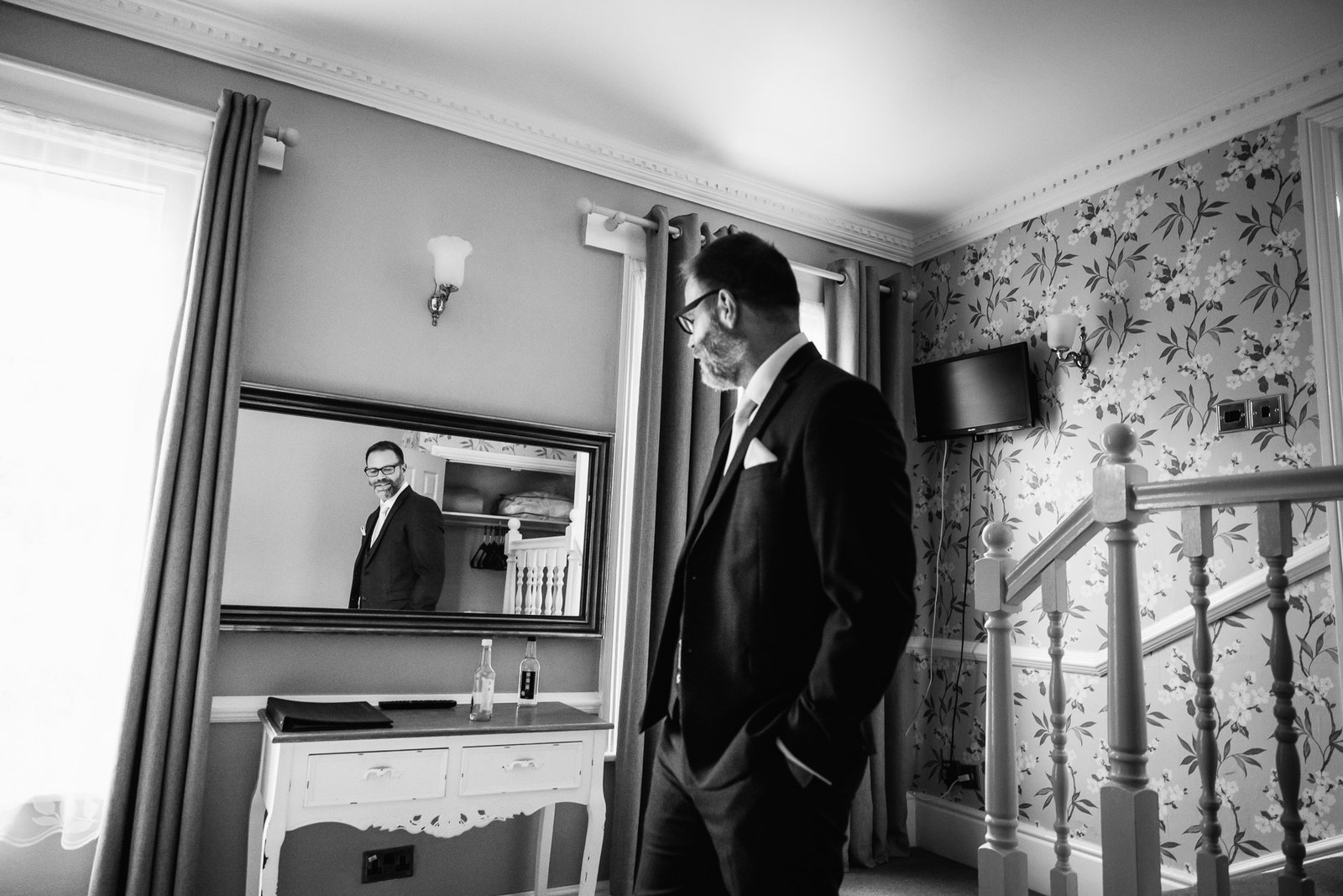 Black and white portrait of the groom by the staircase and dresser