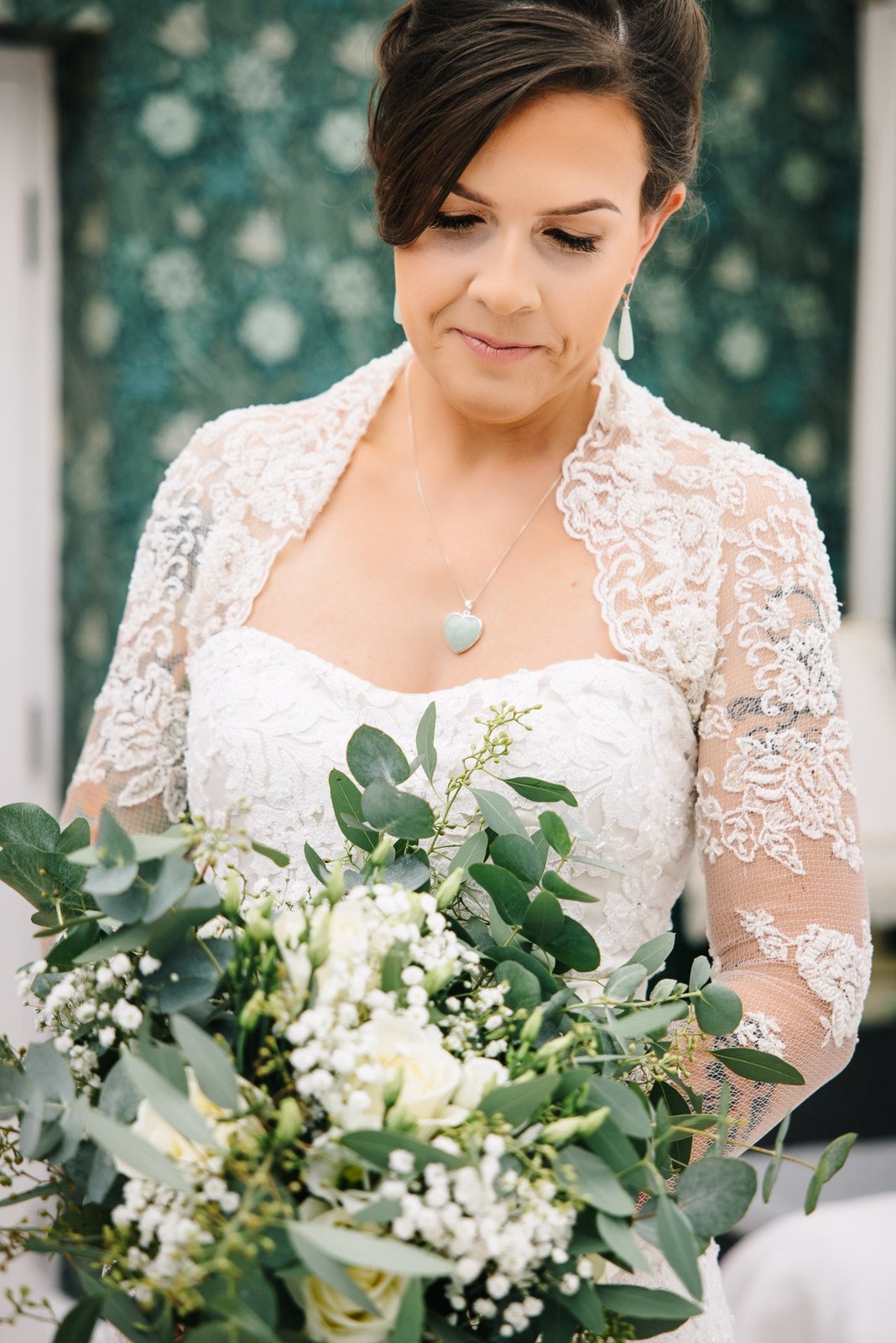 Bride looking down at her lace gown, holding a foliage-rich bouquet
