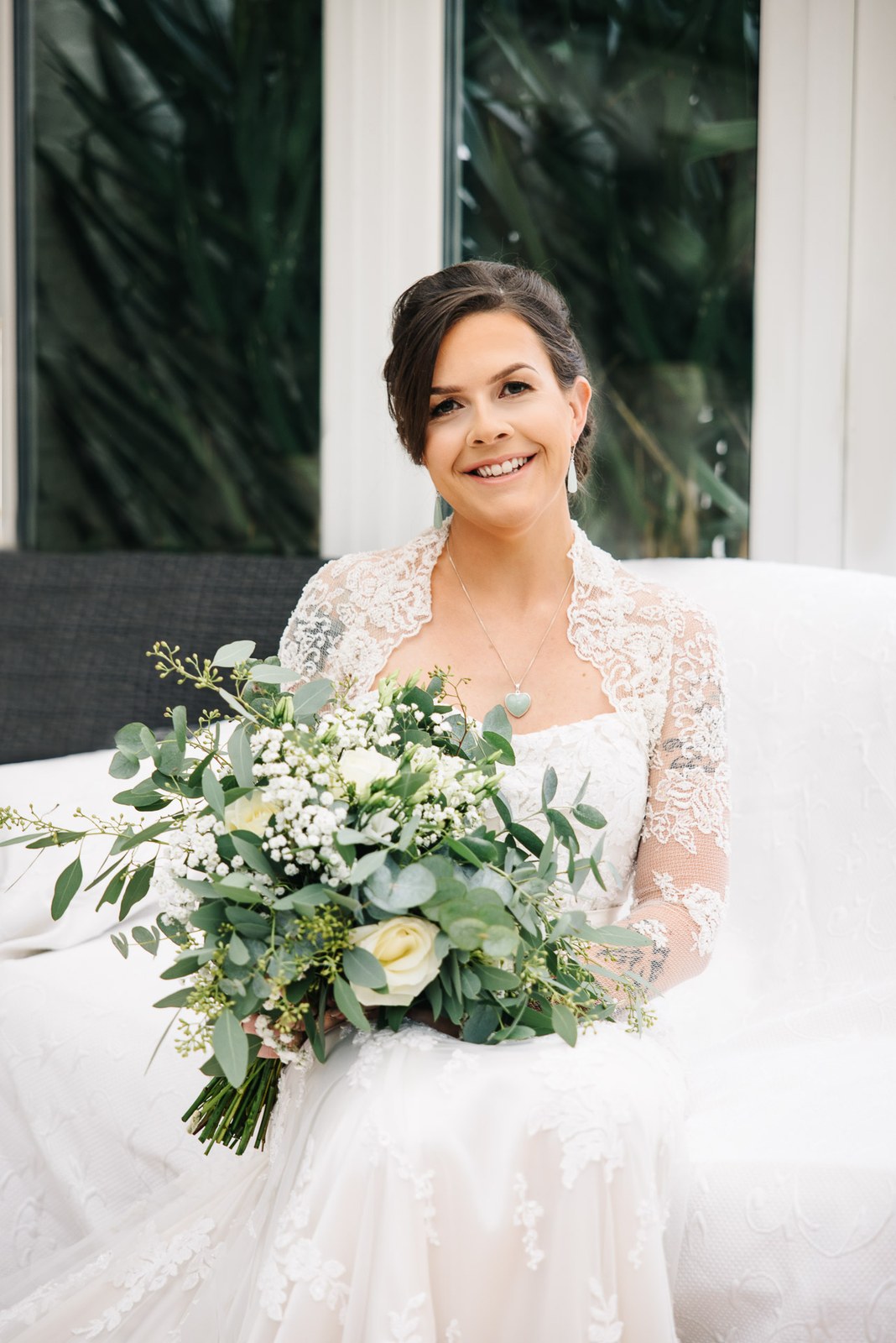 Bride seated and smiling with her white and green bouquet
