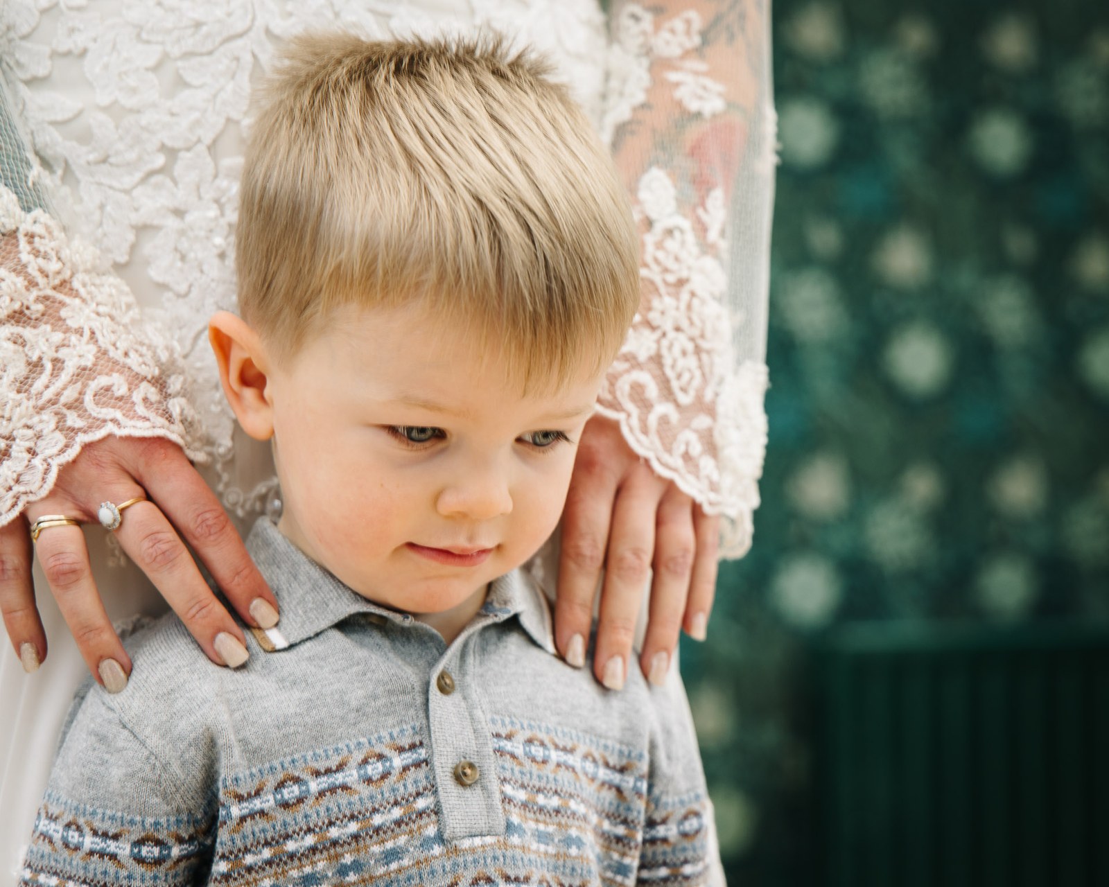 A young page boy with the bride's hands resting on his shoulders
