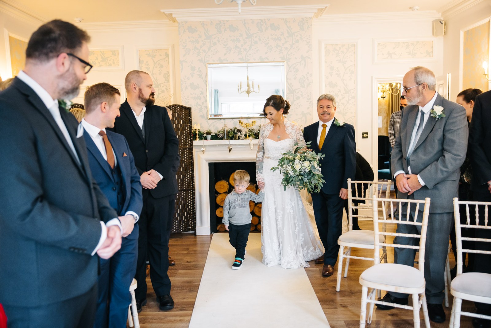 Bride walking down the aisle holding the page boy's hand as the groom waits