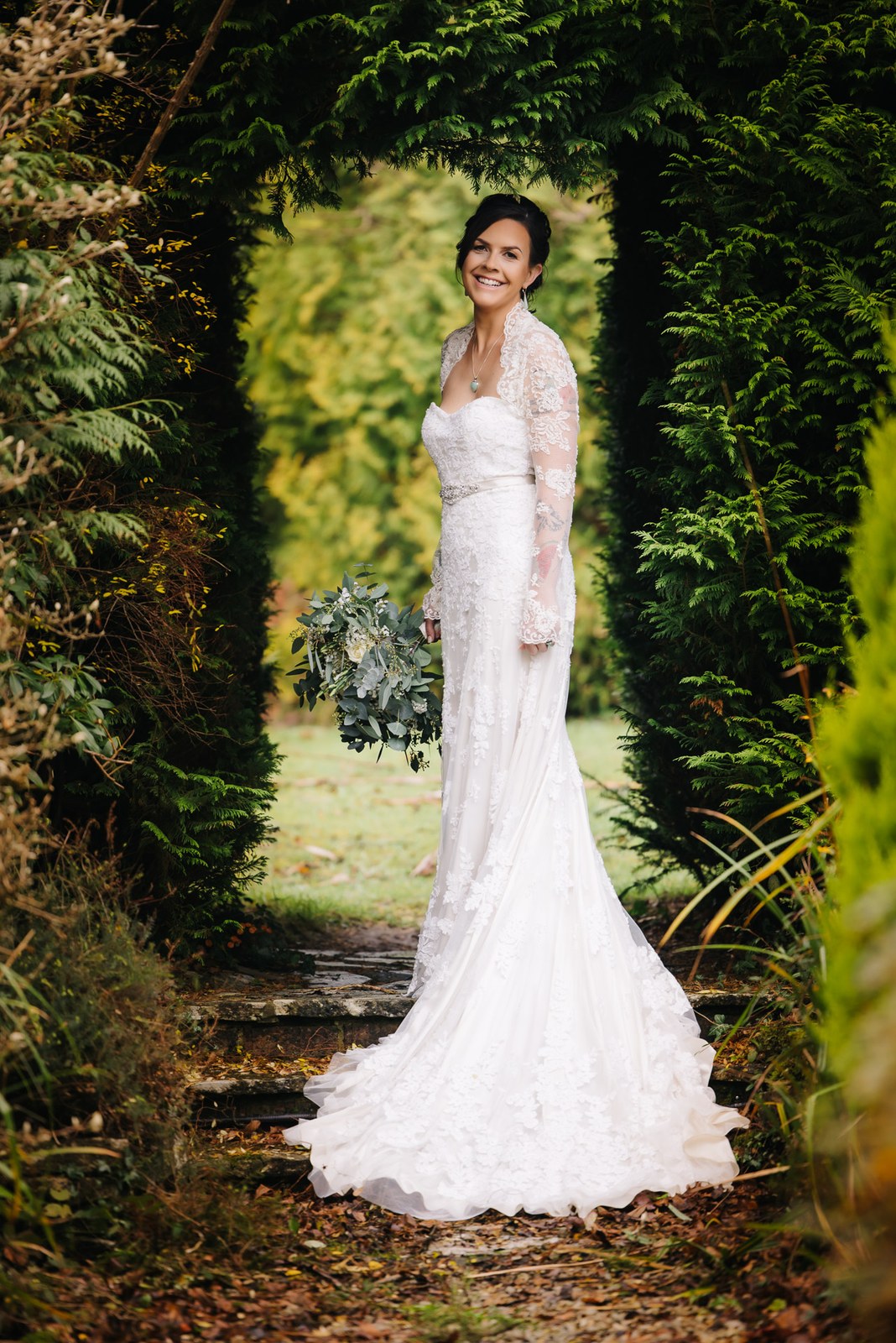 Bride posing in an archway cut through the conifer hedge at Woodlands Lodge Hotel