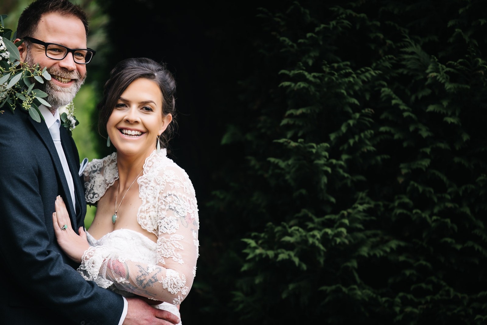 The couple embracing against the deep evergreen backdrop of the grounds at Woodlands Lodge Hotel