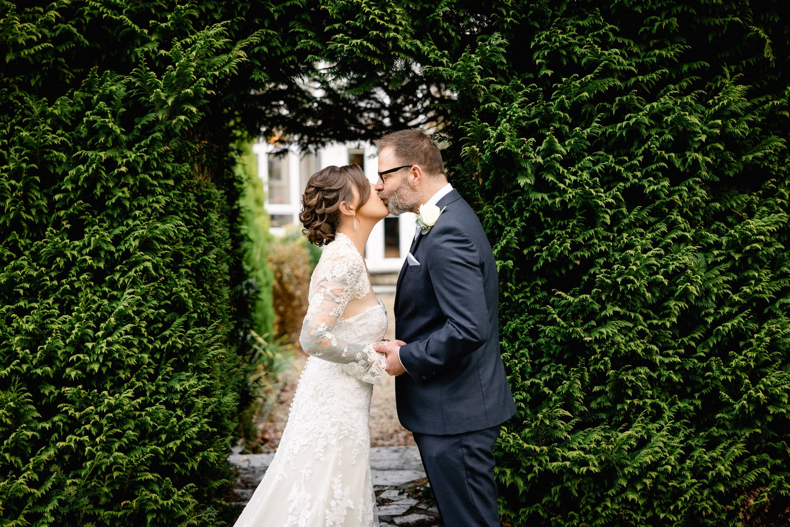 The couple kissing beneath a leafy hedge archway in the Woodlands Lodge Hotel grounds