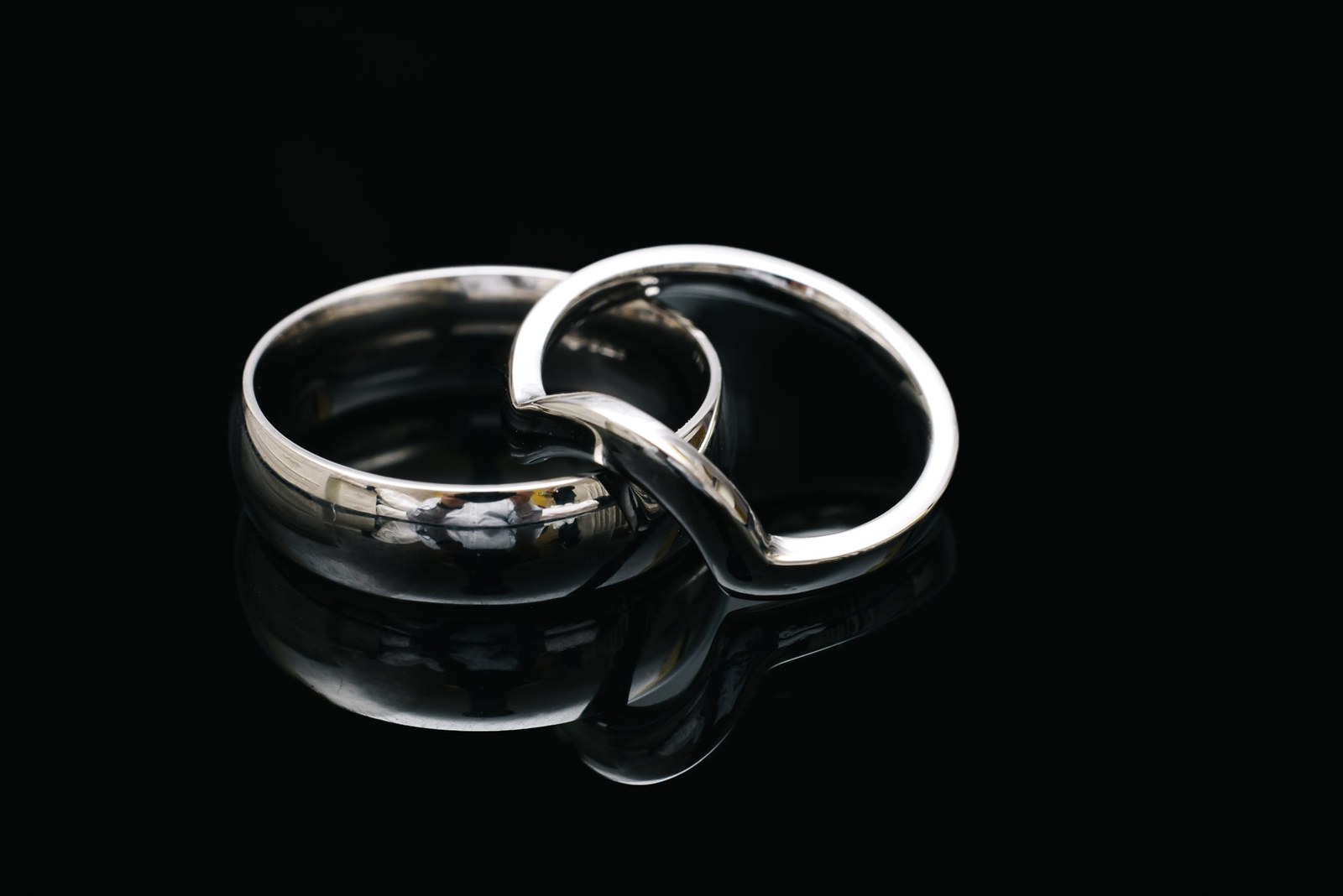 Two wedding bands resting together on a dark reflective surface