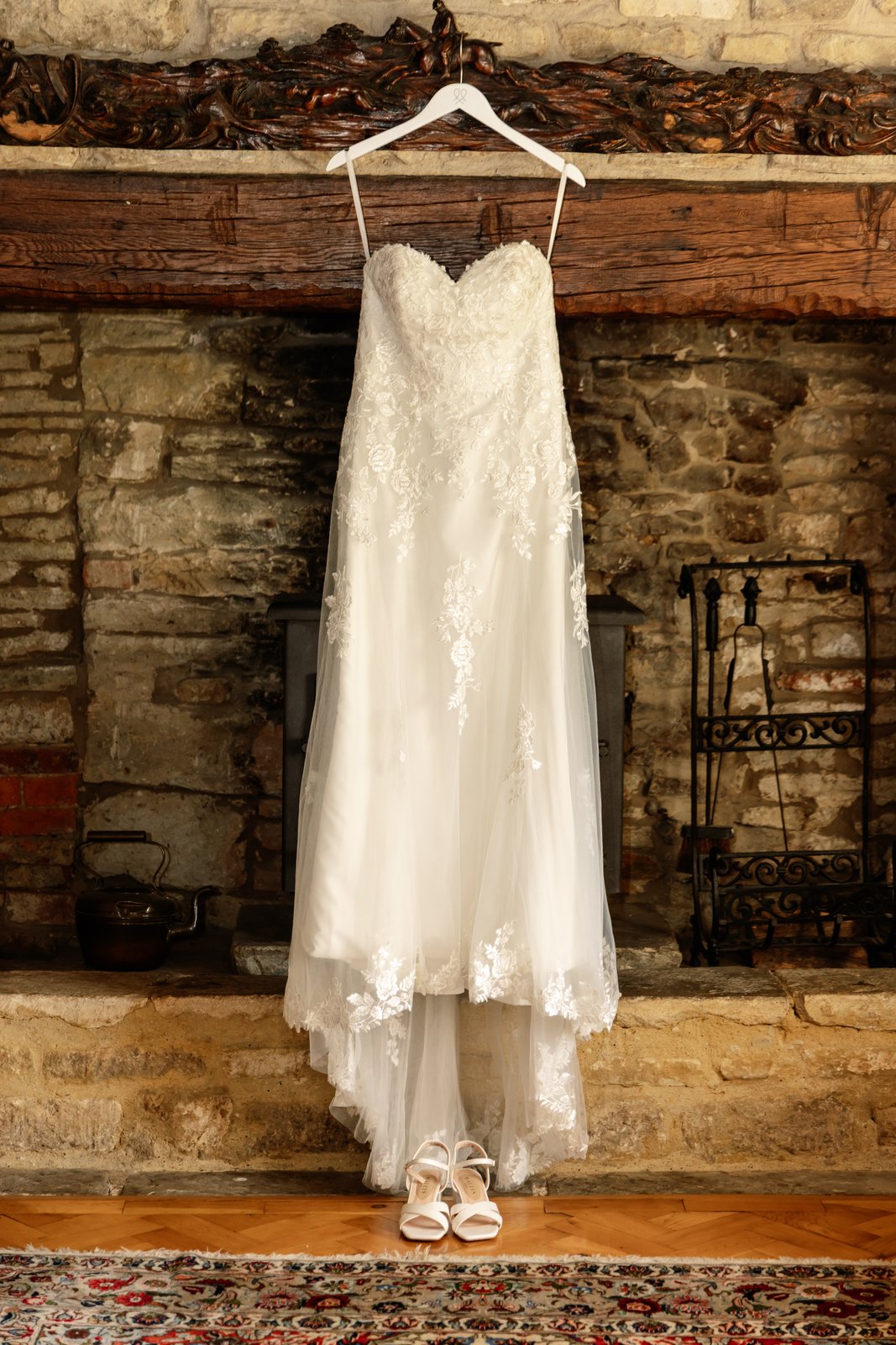 Lace wedding dress hanging against an exposed stone wall at Worton Hall.