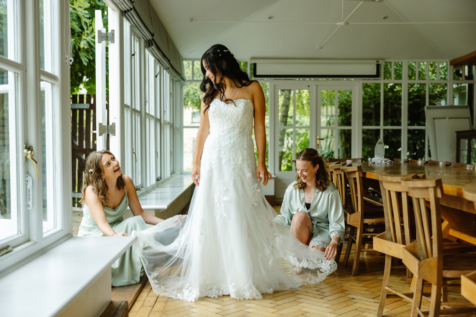 Bride in her gown in a long window-lined room with parquet floors and refectory tables.