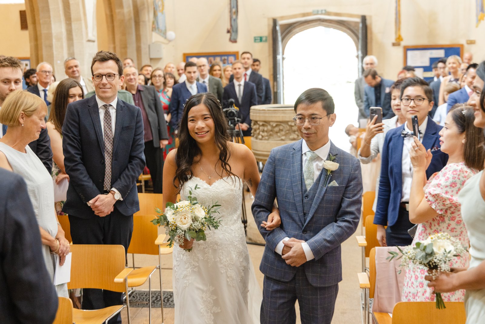 Bride walking down the church aisle on her father's arm as guests turn to watch.