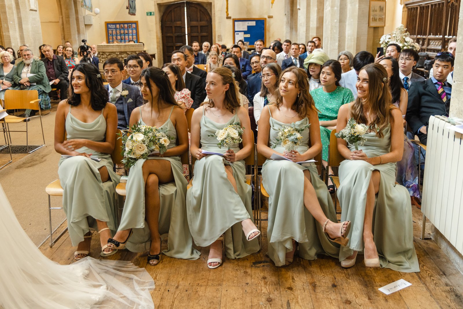Bridesmaids in sage green seated together watching the ceremony from the front row.