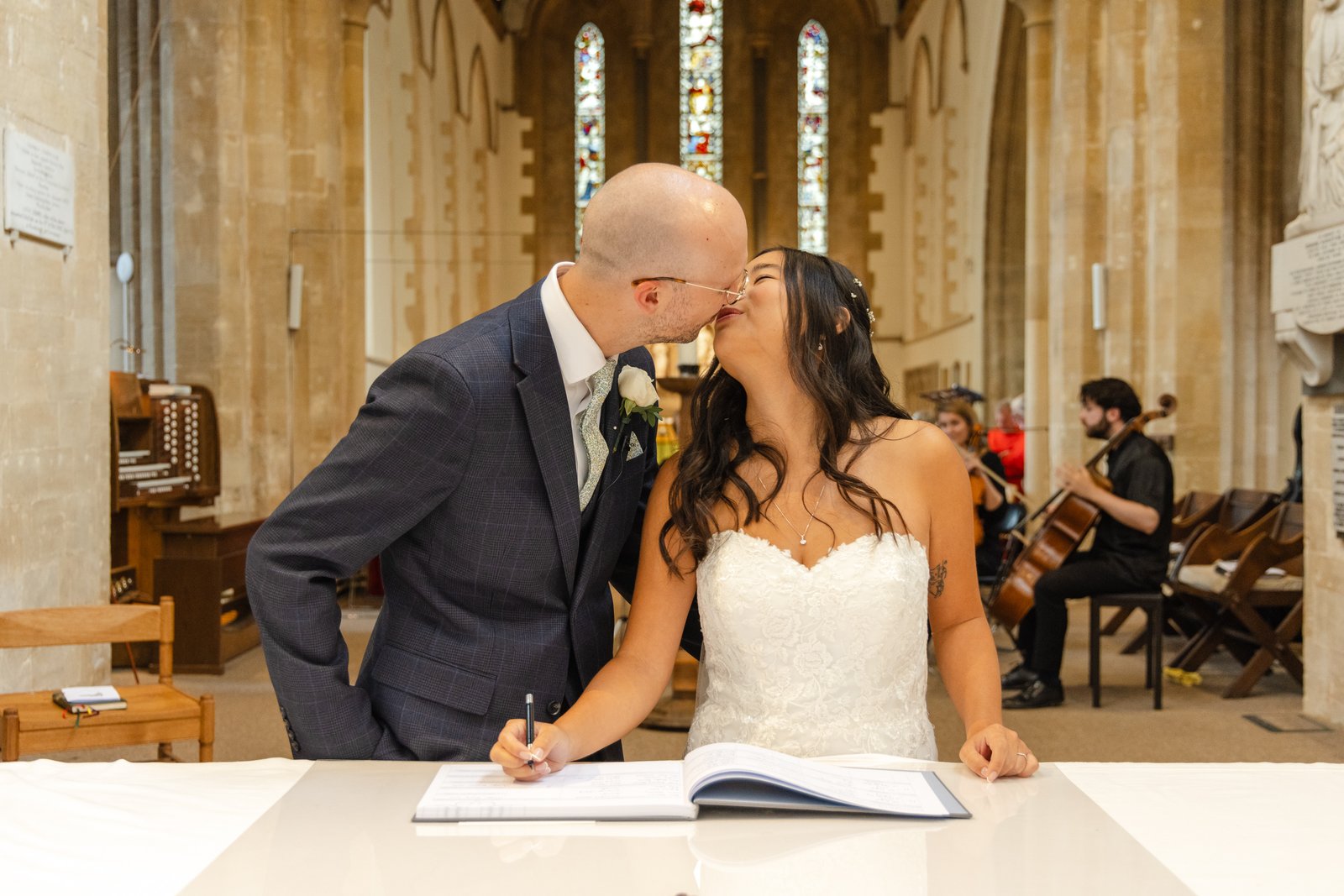 Bride and groom kissing as they sign the marriage register in the church.