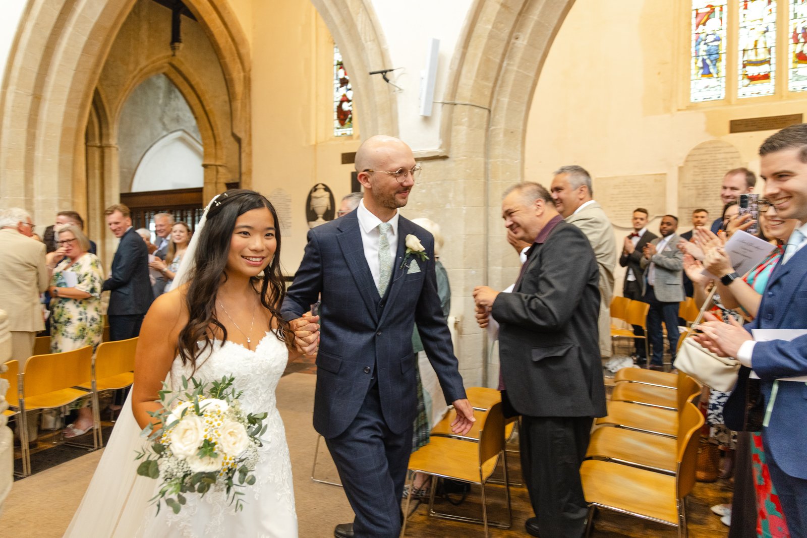 Newly married couple walking back down the aisle to applause from their guests.