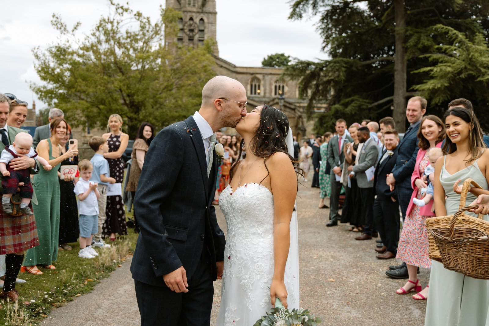 Bride and groom kissing on the church path with guests lining both sides.