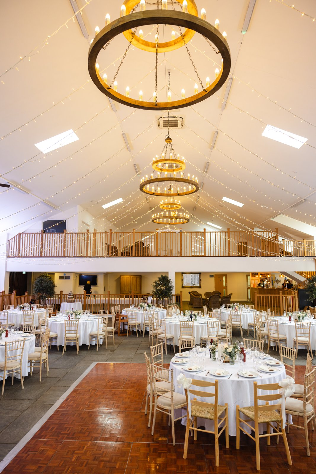 The main hall at Worton Hall set for dinner beneath three lit hoop chandeliers.