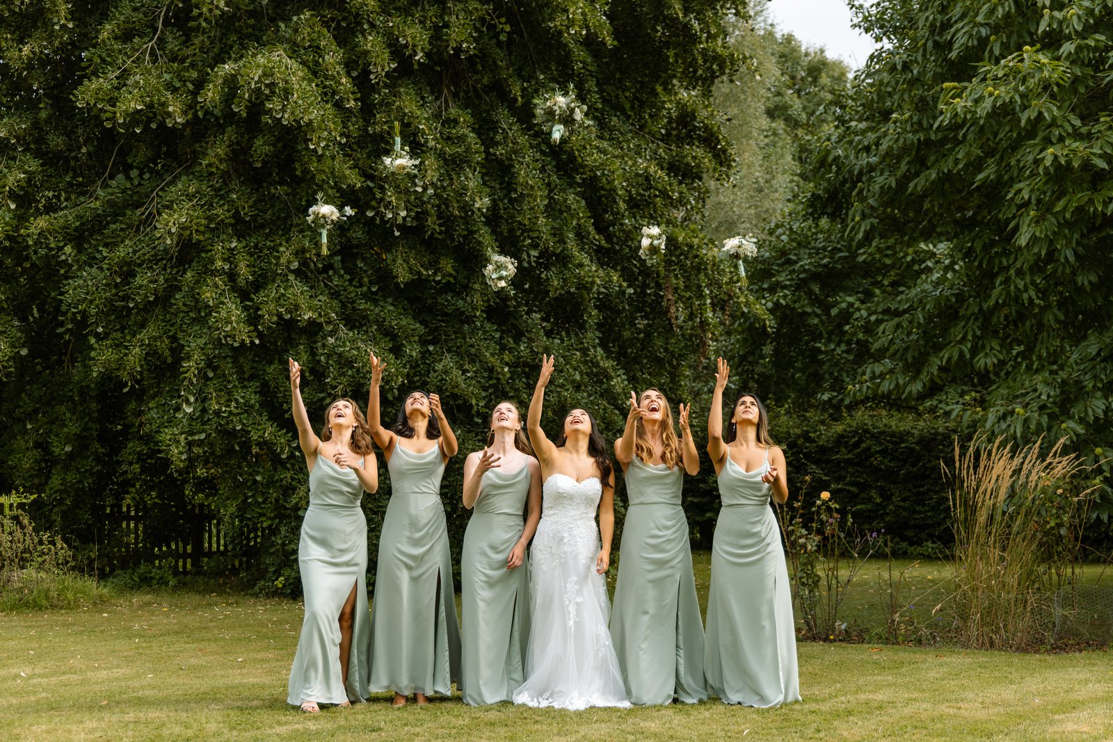 Bridesmaids throwing their bouquets up into the air on the lawn.